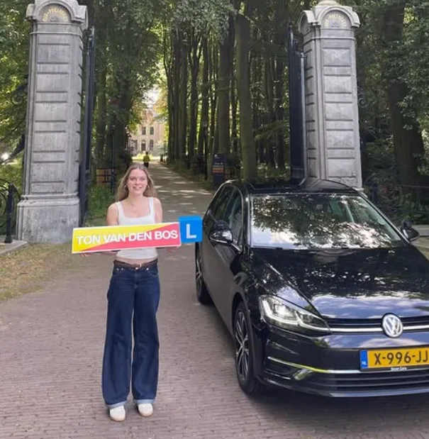 Geslaagde leerling naast de lesauto