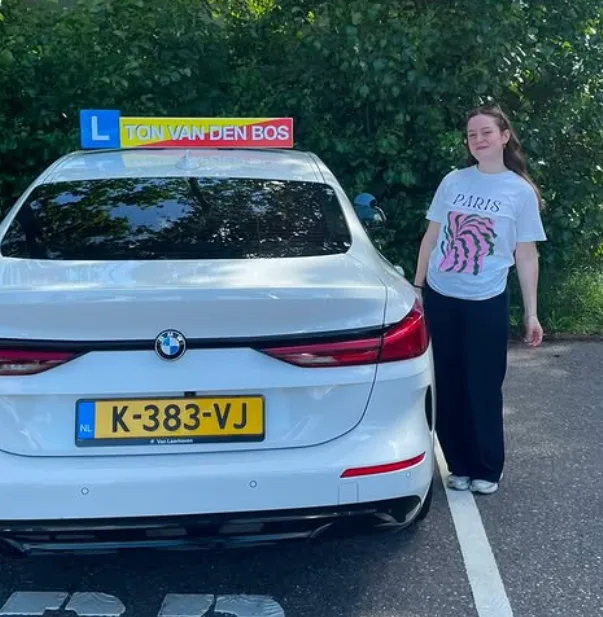 Geslaagde leerling naast de lesauto