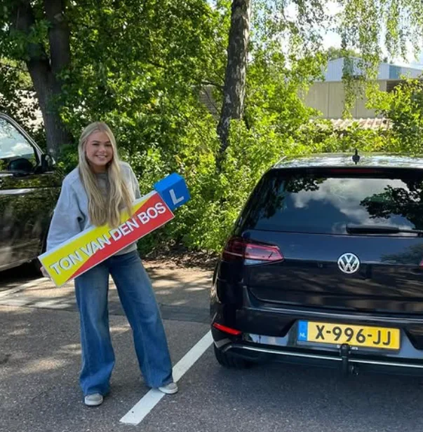 Geslaagde leerling naast de lesauto